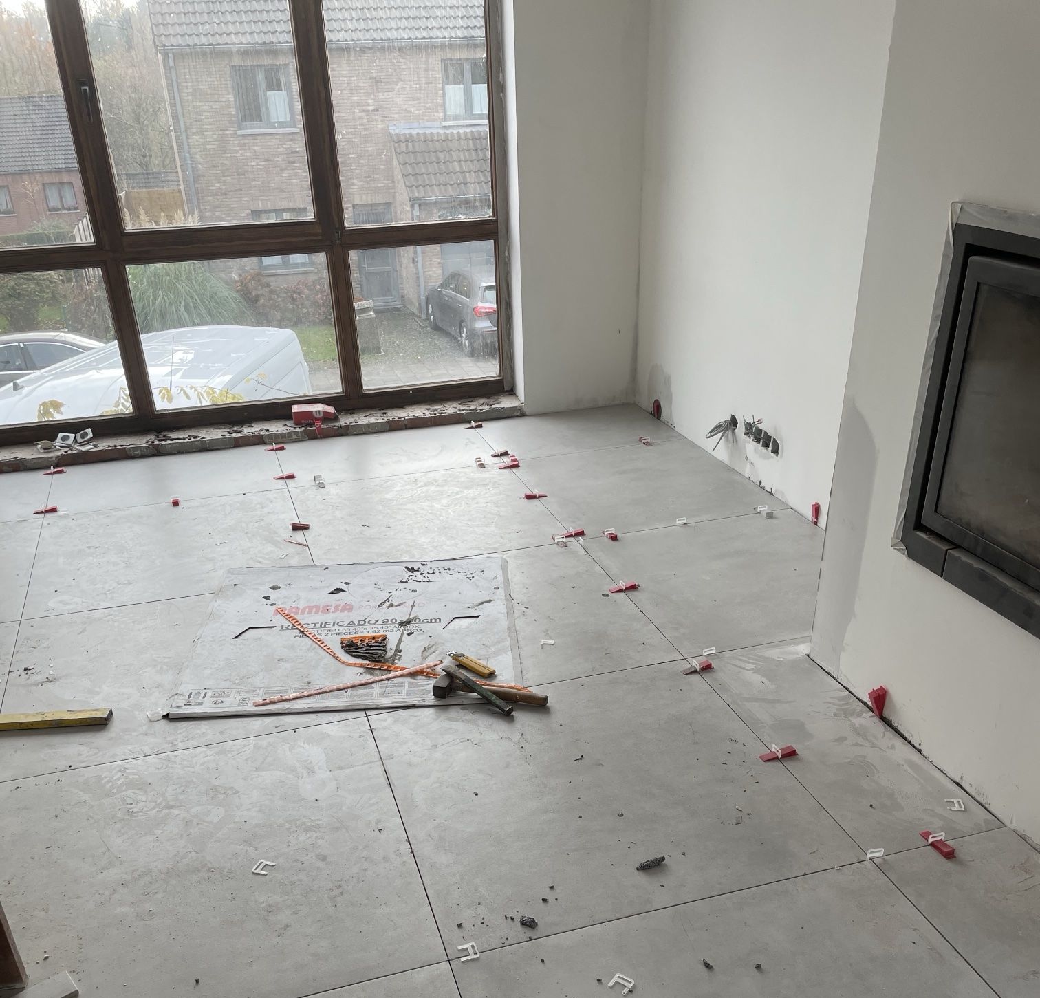 Carrelage grand format en cours de pose devant la baie vitrée et la cheminée