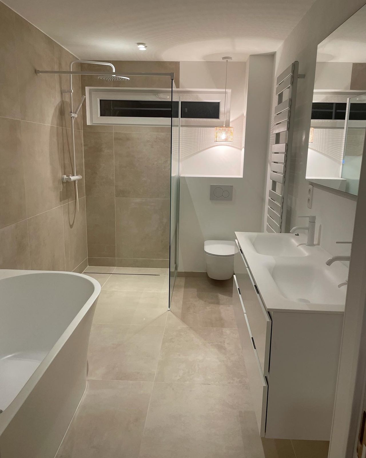 Salle de bain éclairée le soir : douche italienne, WC suspendu et suspension en rotin