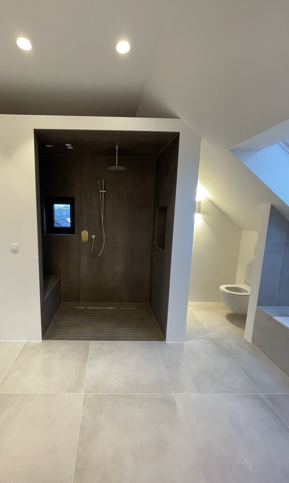 Douche walk-in en carrelage sombre avec banc, niches et robinetterie laiton